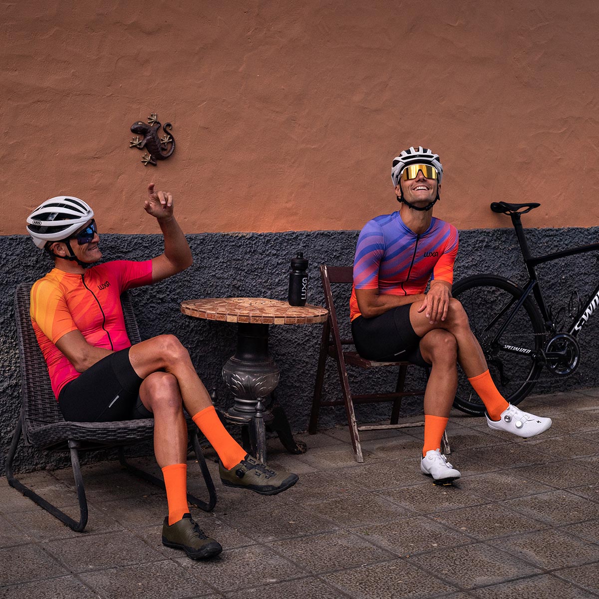 Two cycling friends are smiling when waiting for coffee in the Tenerife small town and wearing Luxa cycling kit from 2023 season